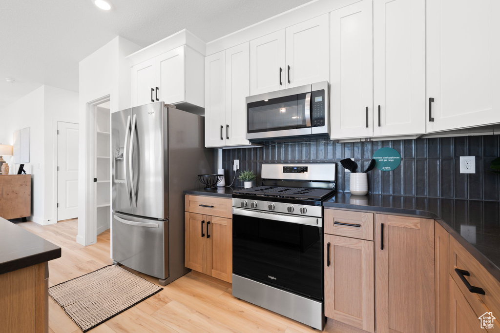 Kitchen featuring appliances with stainless steel finishes, light wood-type flooring, tasteful backsplash, and white cabinetry