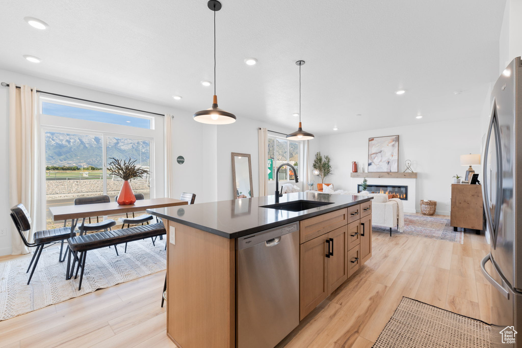 Kitchen with a kitchen island with sink, sink, light hardwood / wood-style flooring, stainless steel appliances, and decorative light fixtures