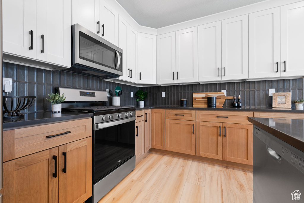 Kitchen featuring decorative backsplash, light wood-type flooring, white cabinetry, and appliances with stainless steel finishes