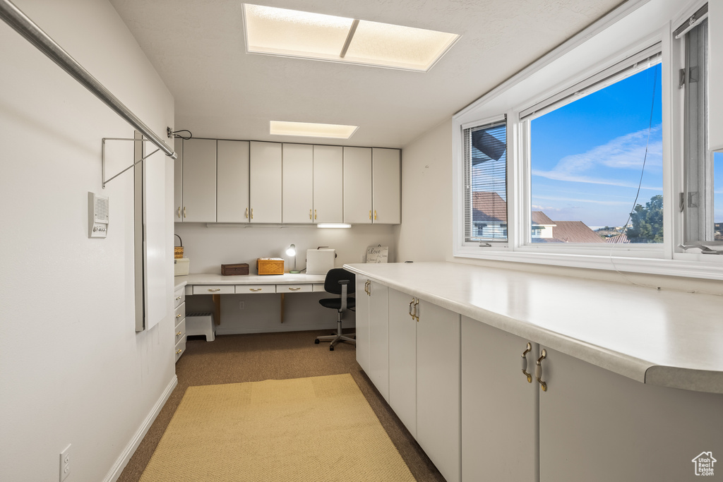 Kitchen with carpet floors, built in desk, and white cabinetry