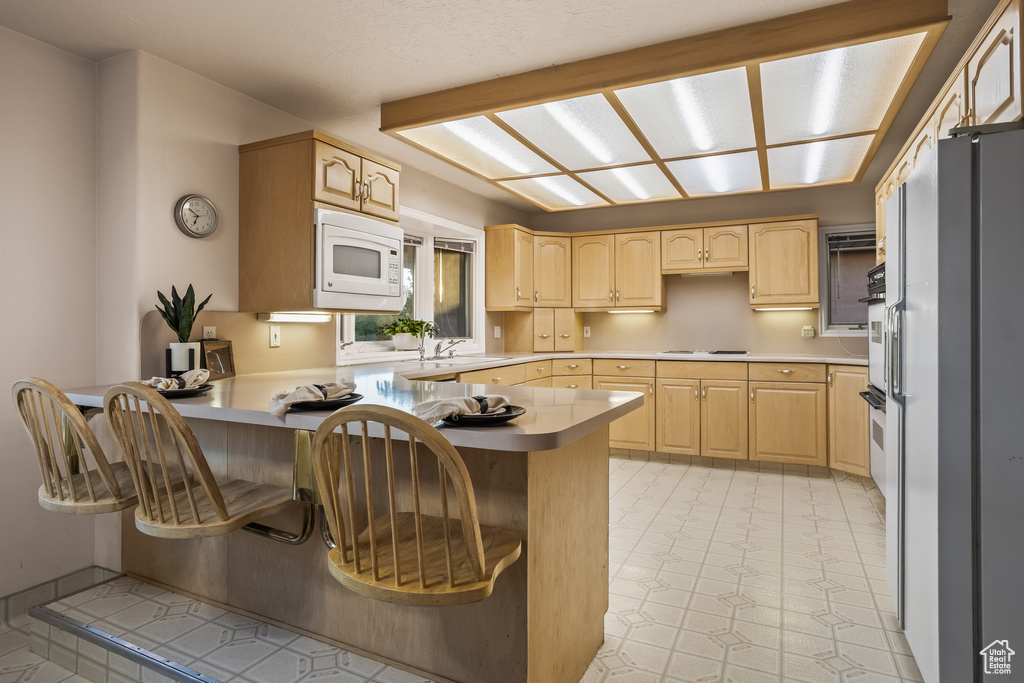 Kitchen featuring kitchen peninsula, white microwave, and light brown cabinets