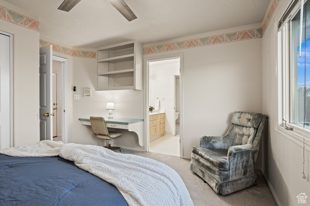 Carpeted bedroom featuring built in desk, connected bathroom, and ceiling fan