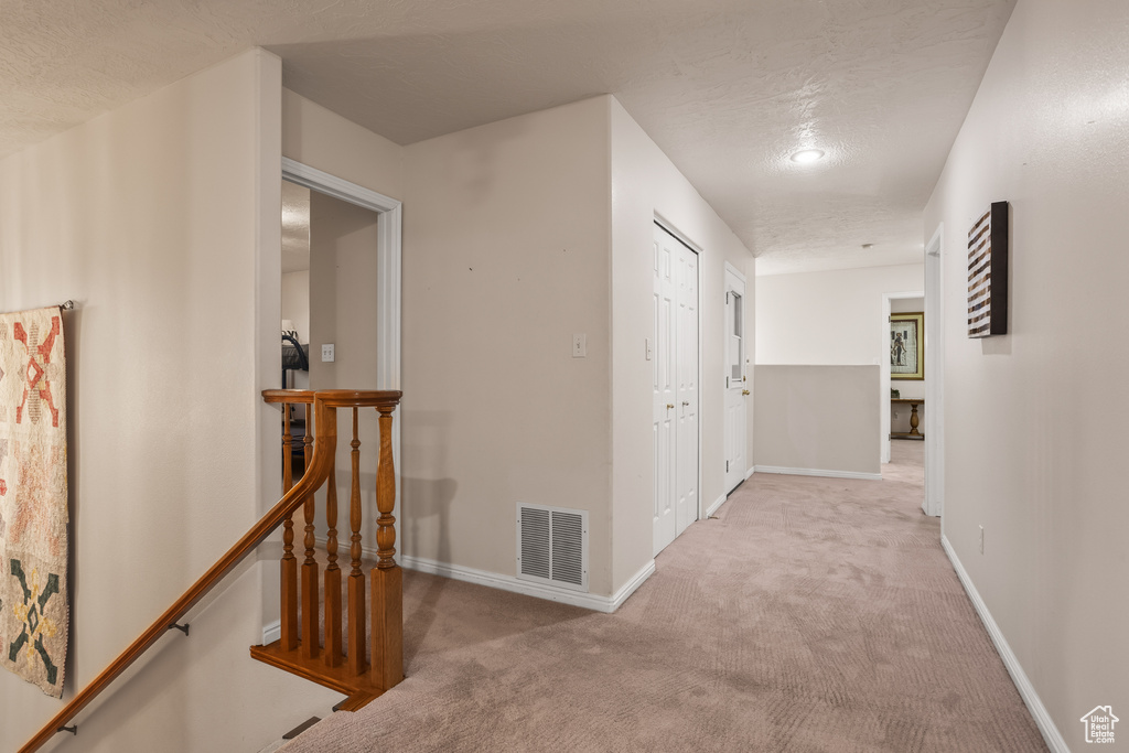 Hall featuring a textured ceiling and light colored carpet