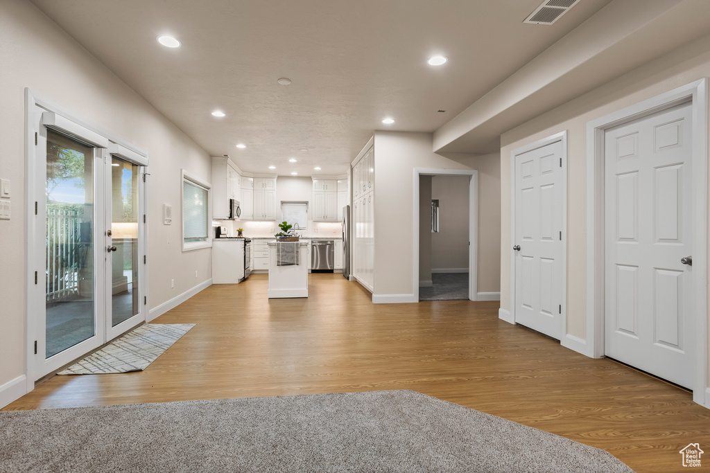 Interior space featuring appliances with stainless steel finishes, white cabinetry, a center island, and light hardwood / wood-style flooring