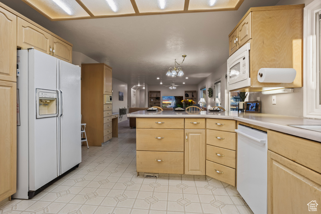 Kitchen with light brown cabinets, hanging light fixtures, kitchen peninsula, white appliances, and an inviting chandelier