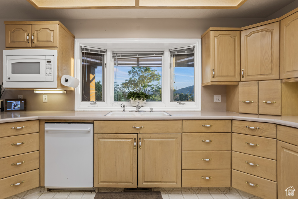 Kitchen featuring light brown cabinetry, sink, and white appliances