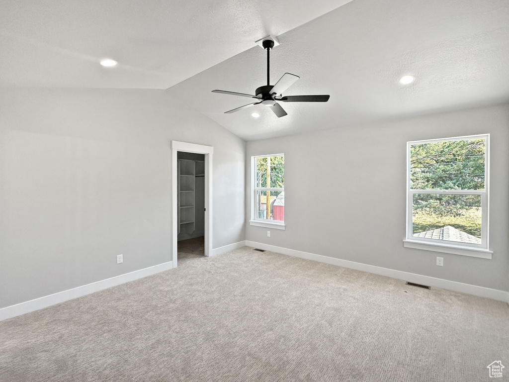 Unfurnished bedroom featuring ceiling fan, light colored carpet, a spacious closet, a closet, and lofted ceiling