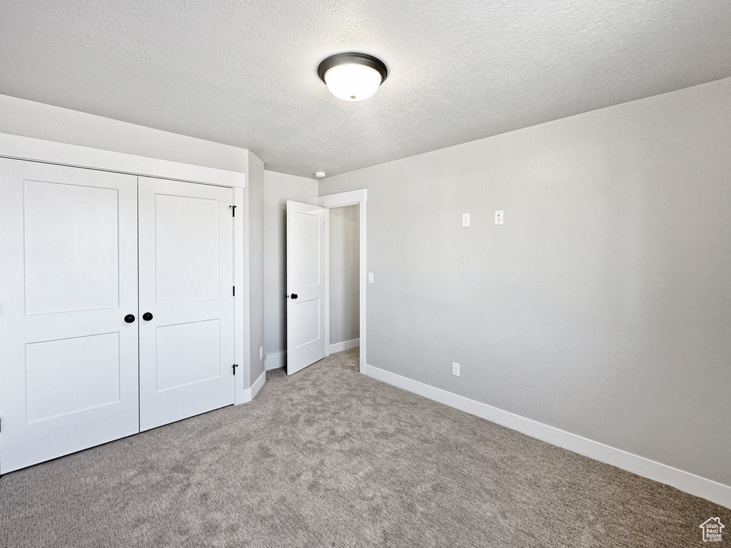 Unfurnished bedroom with light carpet, a textured ceiling, and a closet