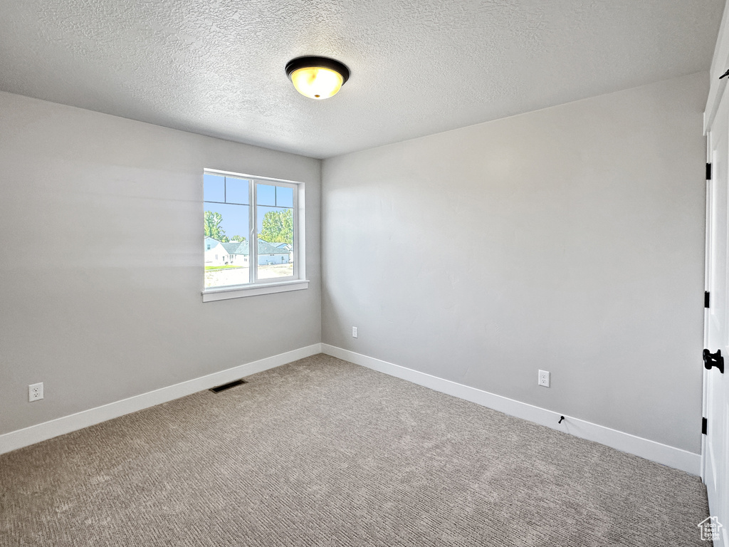 Empty room featuring a textured ceiling and carpet flooring