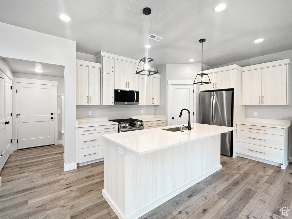 Kitchen with an island with sink, sink, decorative light fixtures, appliances with stainless steel finishes, and light hardwood / wood-style floors