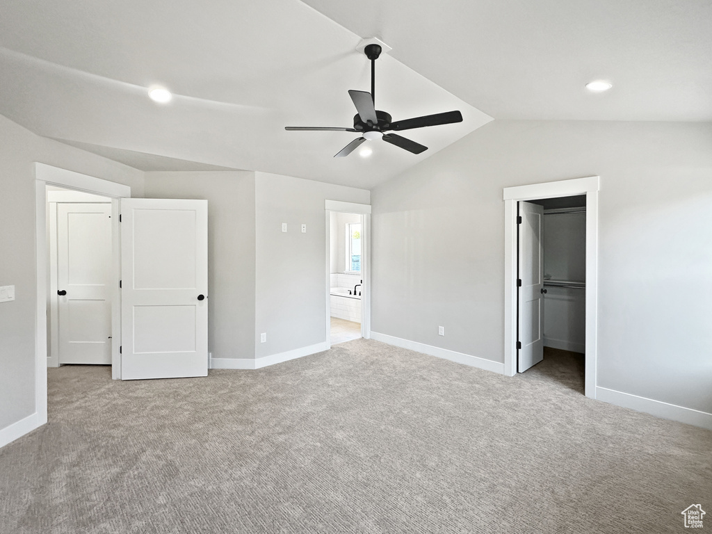 Unfurnished bedroom with lofted ceiling, a spacious closet, ceiling fan, light carpet, and ensuite bath