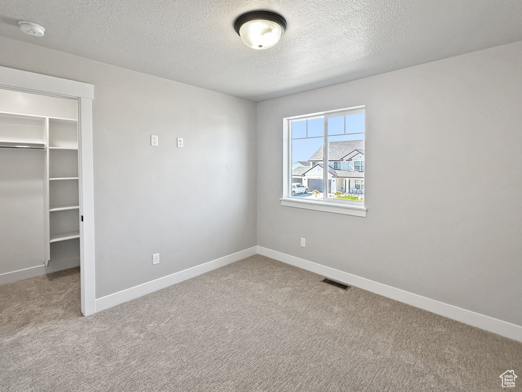 Unfurnished bedroom with light carpet, a walk in closet, a closet, and a textured ceiling