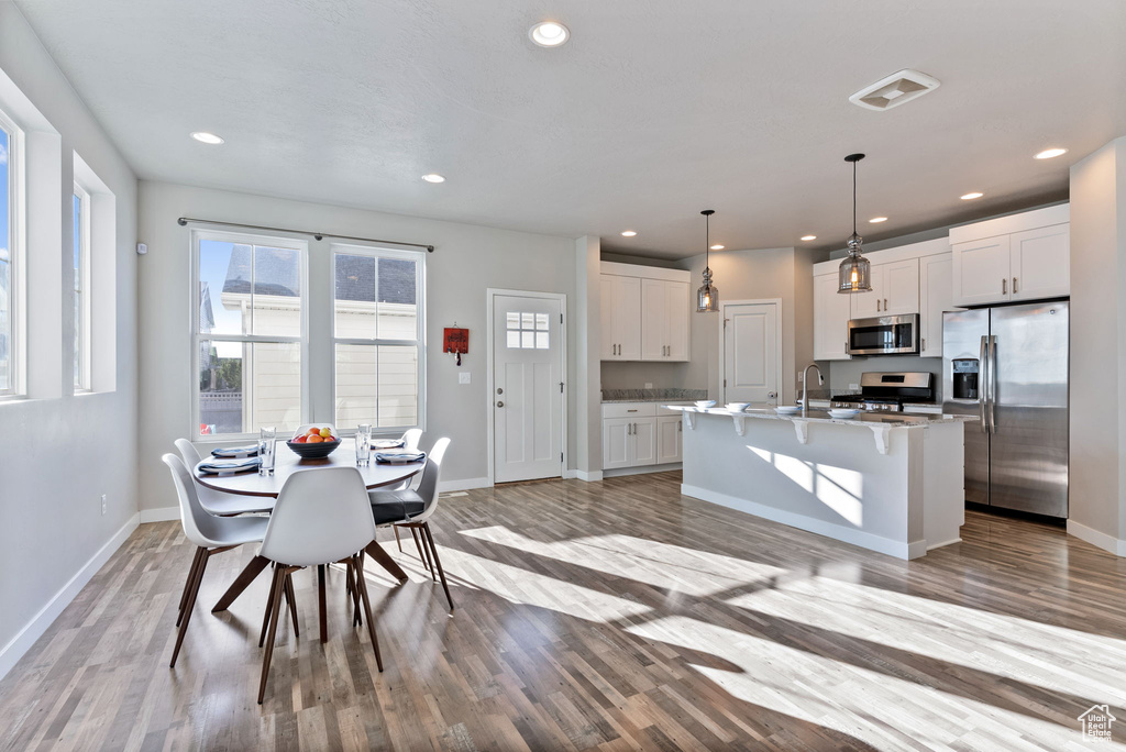 Kitchen with light hardwood / wood-style flooring, white cabinets, appliances with stainless steel finishes, and a kitchen island with sink