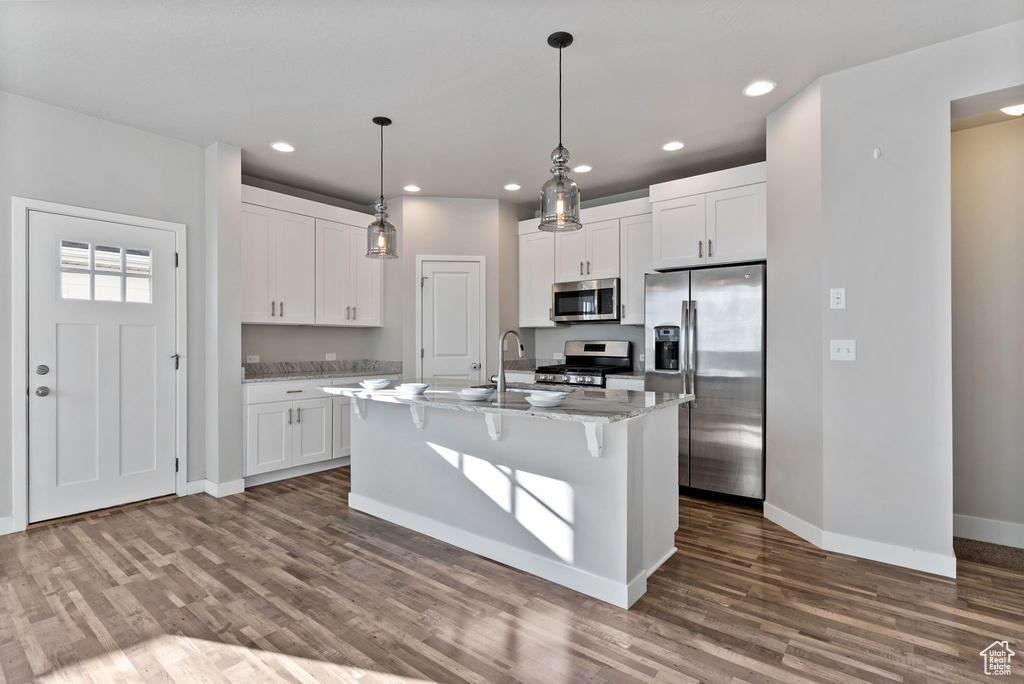 Kitchen with white cabinets, a center island with sink, appliances with stainless steel finishes, and hardwood / wood-style flooring