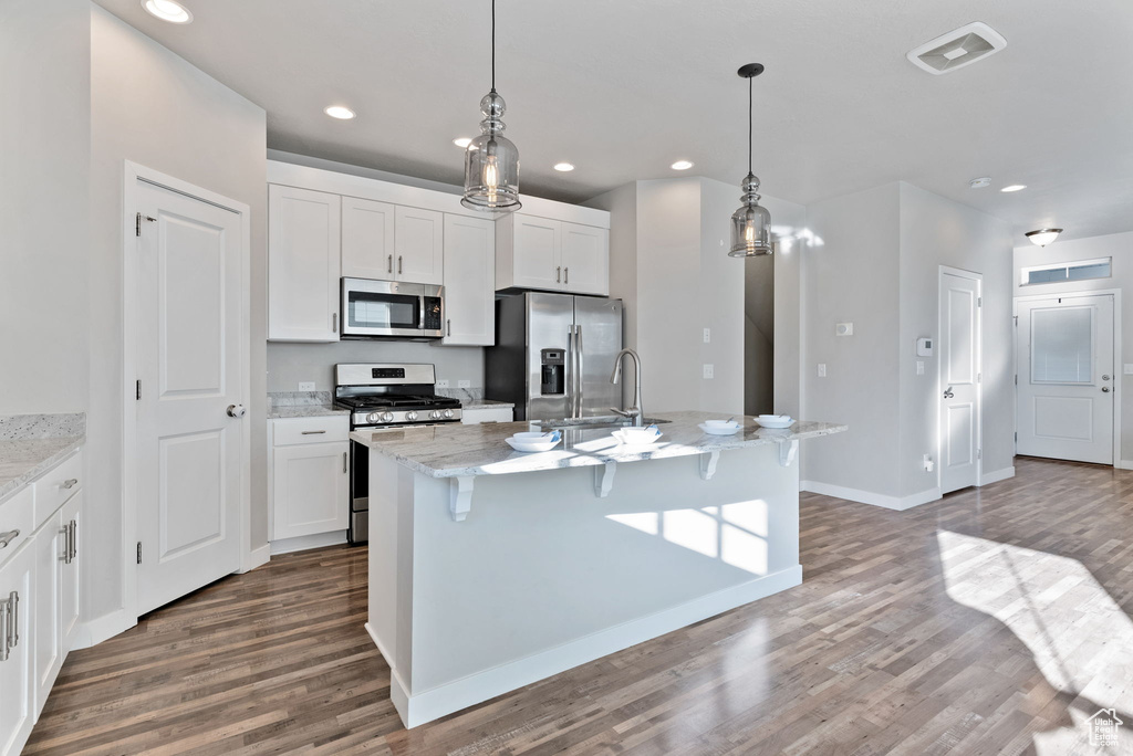 Kitchen with white cabinets, a center island with sink, stainless steel appliances, and hardwood / wood-style floors