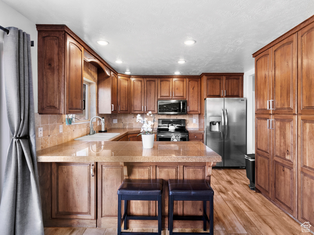 Kitchen featuring sink, kitchen peninsula, appliances with stainless steel finishes, a breakfast bar area, and light wood-type flooring