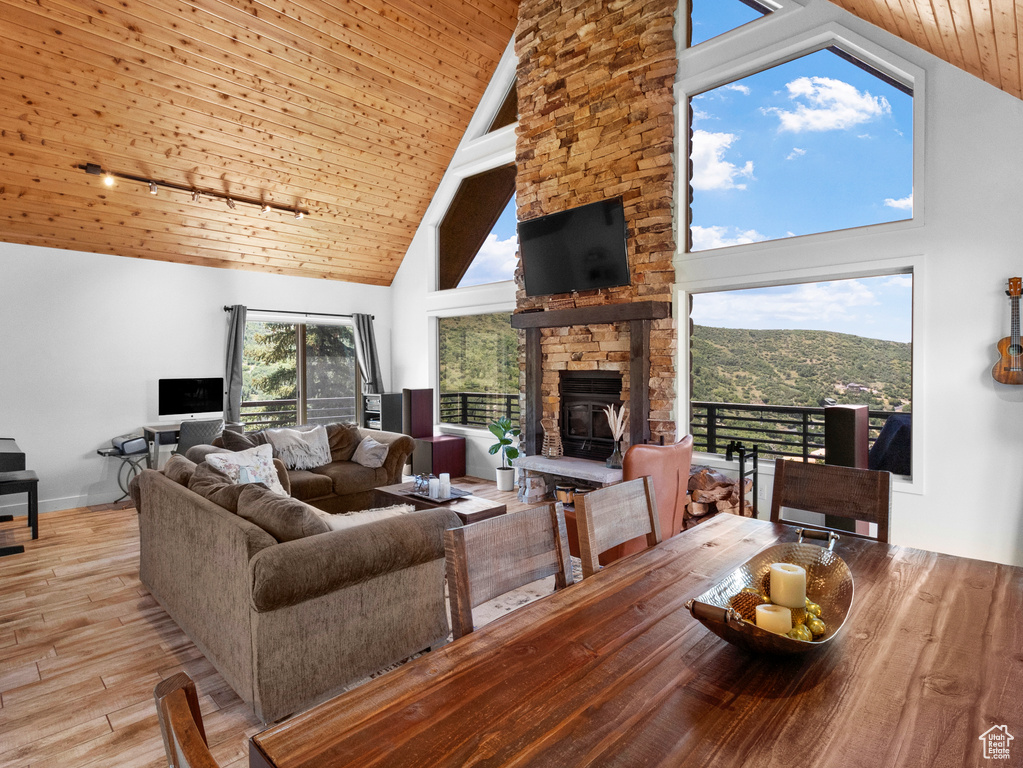 Living room with light hardwood / wood-style floors, wooden ceiling, a stone fireplace, and high vaulted ceiling