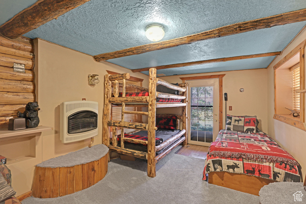 Carpeted bedroom featuring a textured ceiling, beam ceiling, log walls, and heating unit