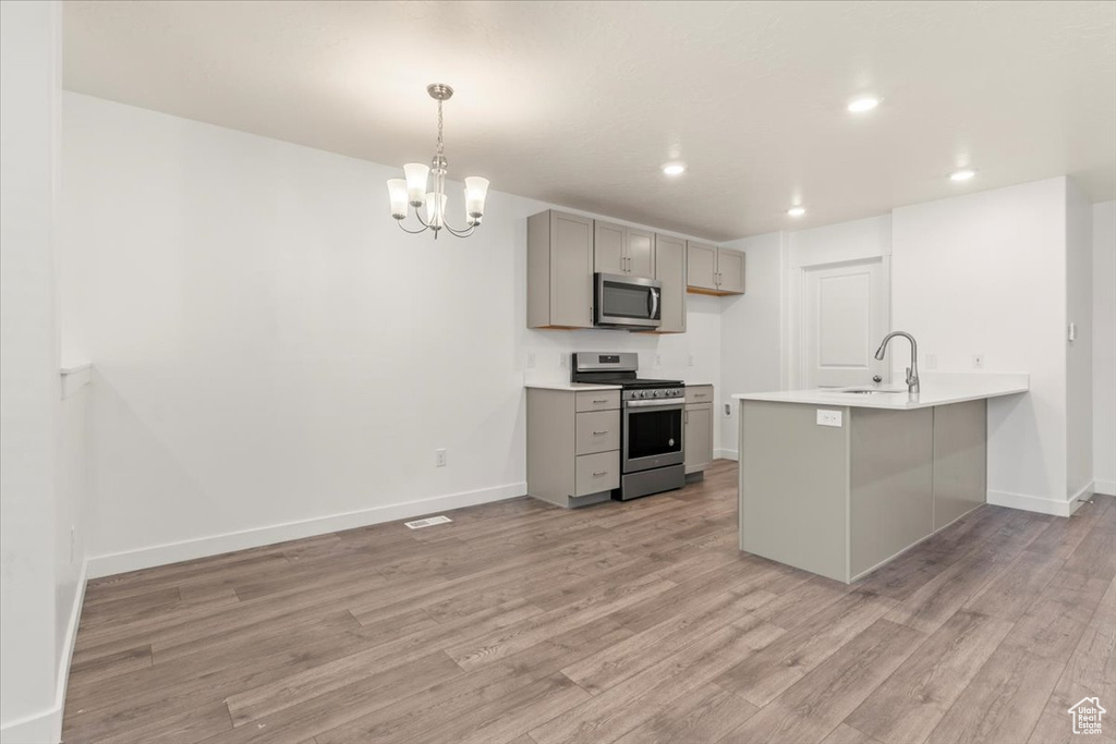 Kitchen featuring pendant lighting, stainless steel appliances, light hardwood / wood-style floors, and gray cabinetry