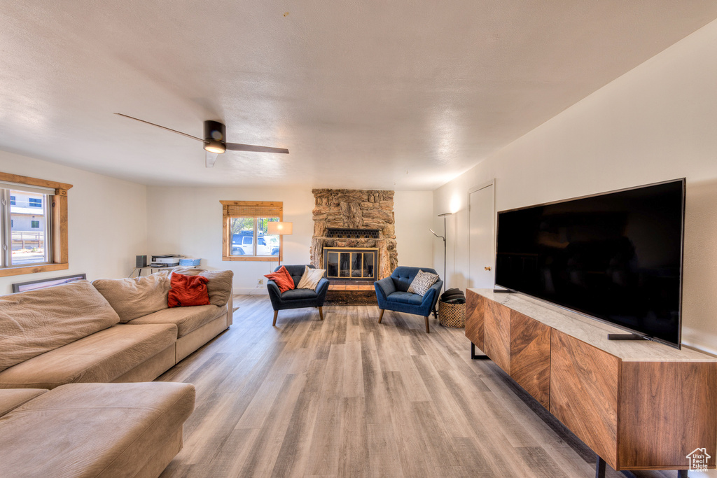 Living room featuring ceiling fan, a stone fireplace, light hardwood / wood-style flooring, and a wealth of natural light
