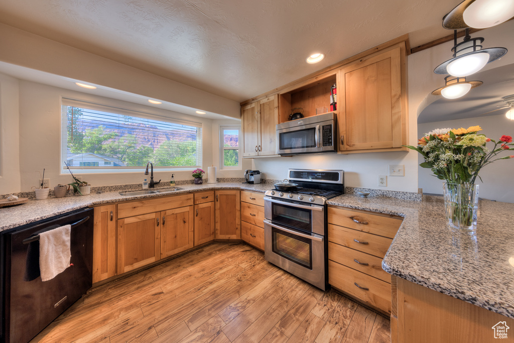 Kitchen with light wood-type flooring, sink, stainless steel appliances, and light stone counters