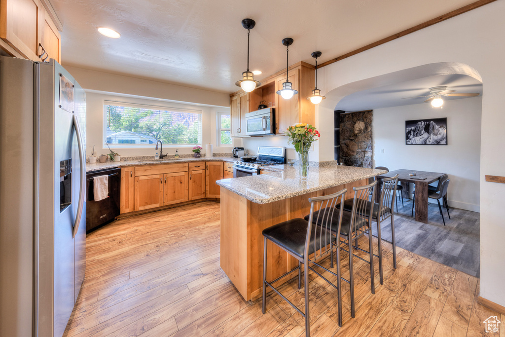 Kitchen featuring a kitchen bar, appliances with stainless steel finishes, kitchen peninsula, and light hardwood / wood-style flooring