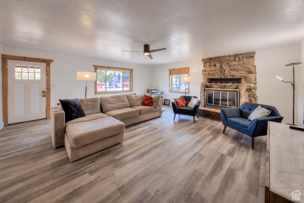 Living room featuring wood-type flooring, a stone fireplace, and ceiling fan