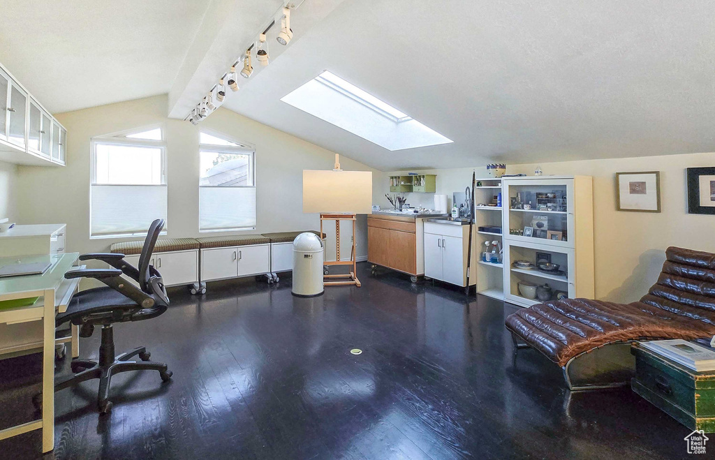 Office space with vaulted ceiling with skylight and dark wood-type flooring