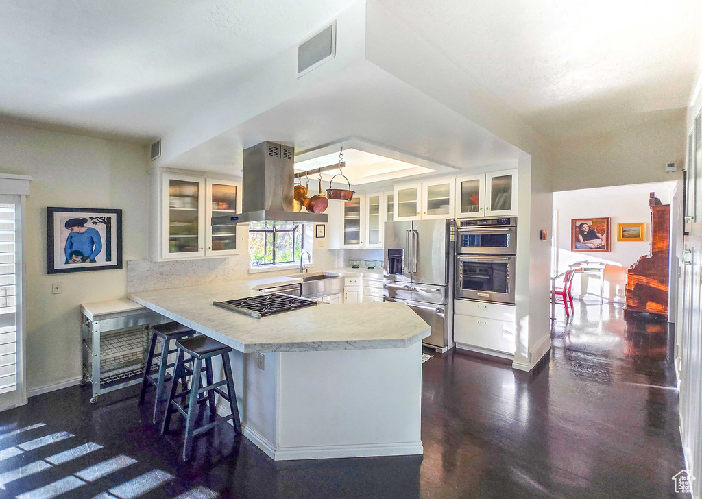 Kitchen featuring a breakfast bar, white cabinetry, appliances with stainless steel finishes, island range hood, and kitchen peninsula