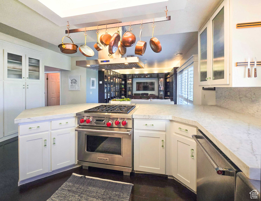 Kitchen with kitchen peninsula, white cabinets, stainless steel appliances, and exhaust hood