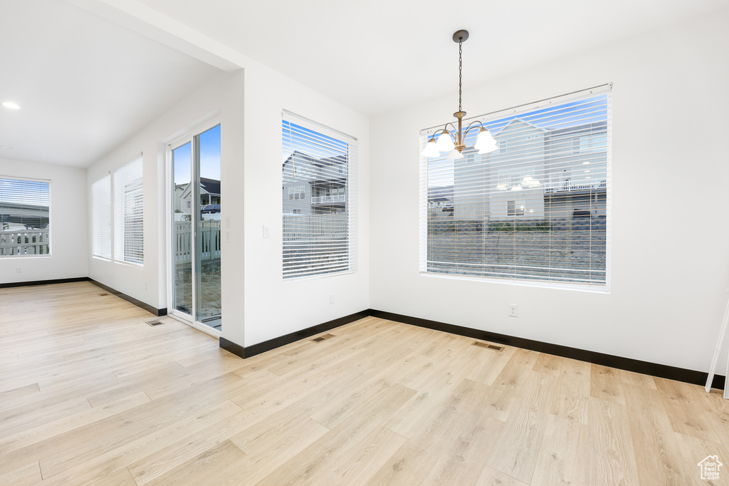 Unfurnished dining area featuring an inviting chandelier, light hardwood / wood-style flooring, and a wealth of natural light