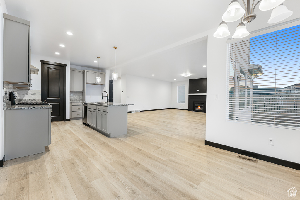 Kitchen with backsplash, pendant lighting, gray cabinets, light hardwood / wood-style flooring, and a kitchen island with sink