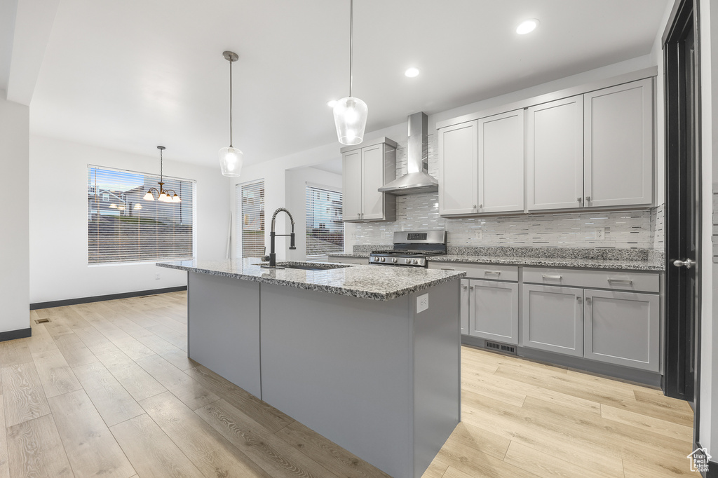 Kitchen featuring an island with sink, wall chimney exhaust hood, pendant lighting, gas range, and sink