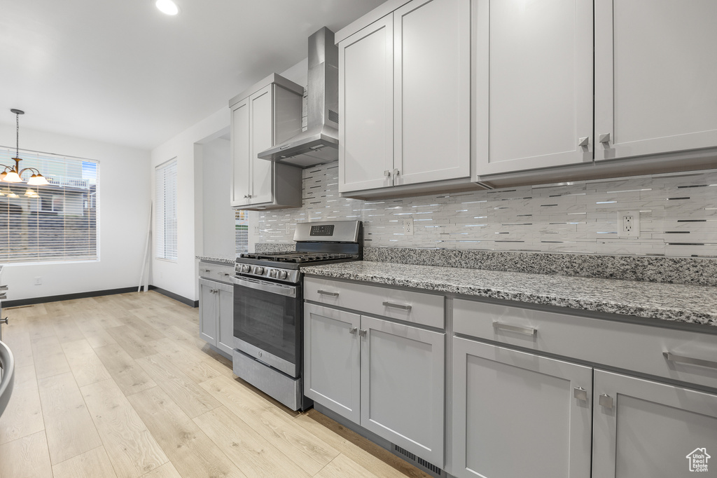 Kitchen with gray cabinetry, light stone counters, light hardwood / wood-style flooring, gas stove, and wall chimney range hood