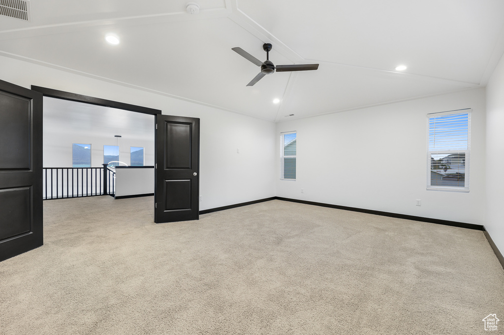 Carpeted empty room featuring ceiling fan, vaulted ceiling, and a wealth of natural light