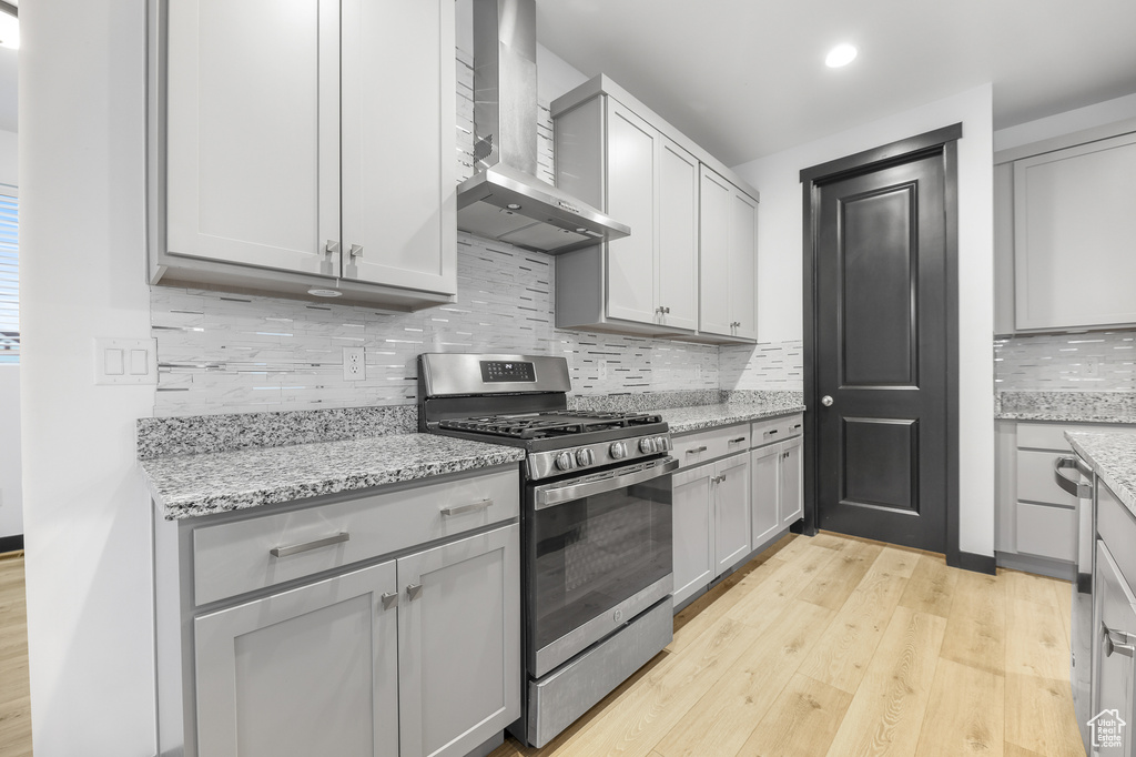 Kitchen with light hardwood / wood-style flooring, wall chimney range hood, gray cabinets, gas stove, and decorative backsplash