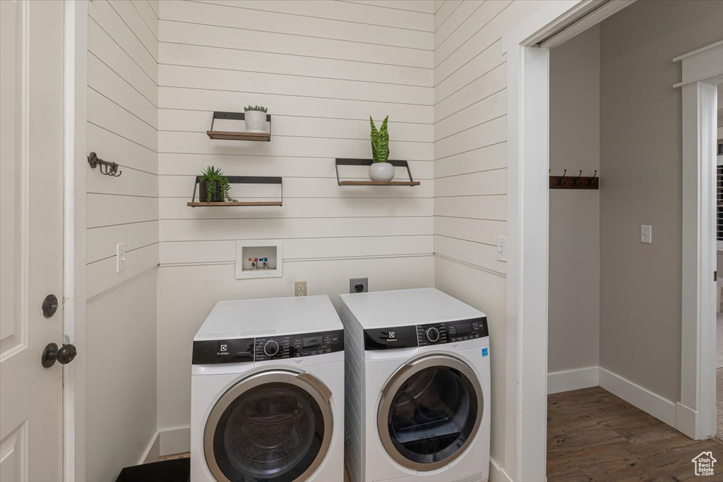 Washroom with wooden walls, washer and clothes dryer, and dark wood-type flooring