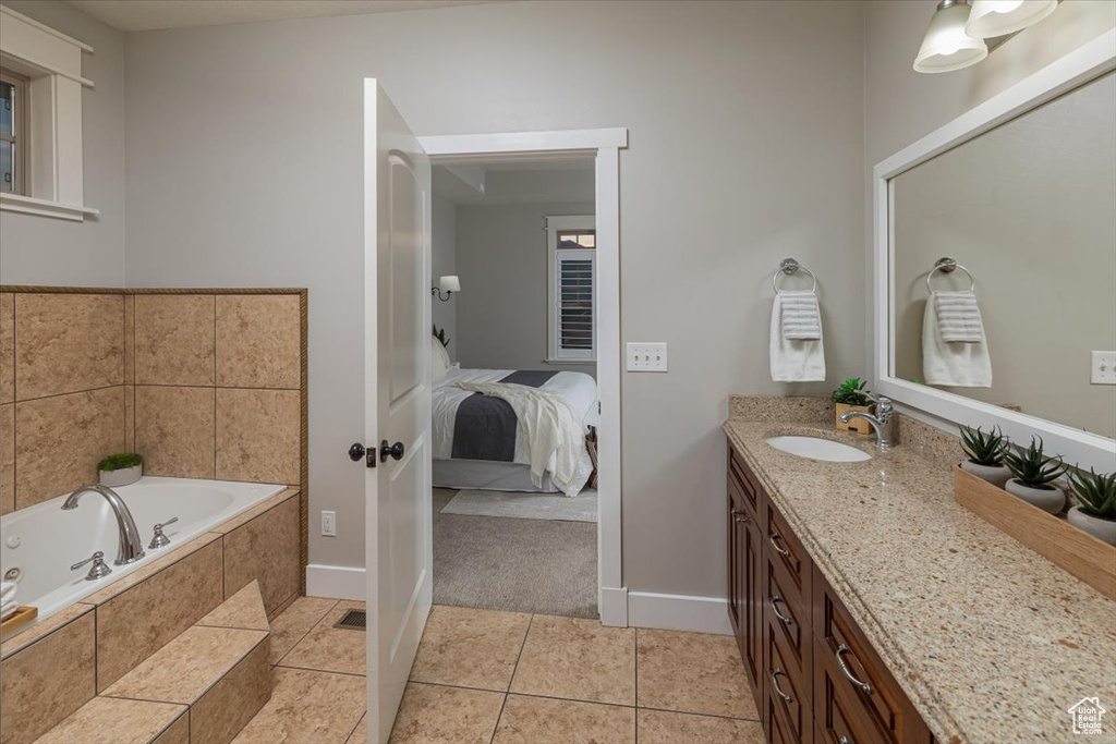 Bathroom with a relaxing tiled tub, vanity, and tile patterned flooring