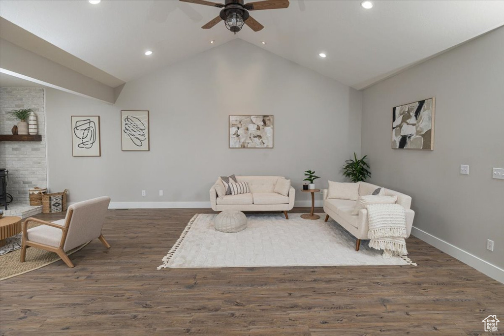 Living room featuring lofted ceiling, ceiling fan, dark wood-type flooring, and a wood stove