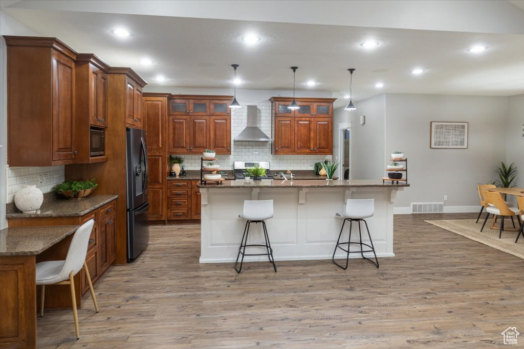 Kitchen with a kitchen island with sink, a kitchen breakfast bar, pendant lighting, and wall chimney range hood