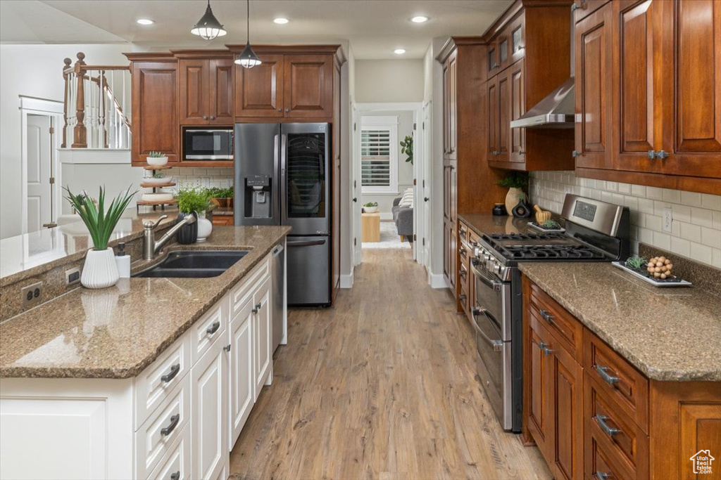 Kitchen featuring light stone counters, white cabinets, hanging light fixtures, light hardwood / wood-style flooring, and appliances with stainless steel finishes