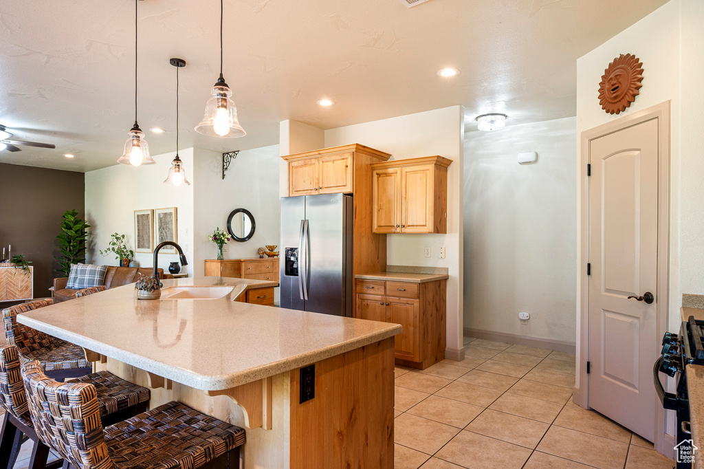 Kitchen featuring an island with sink, decorative light fixtures, stainless steel refrigerator with ice dispenser, a kitchen breakfast bar, and white range with gas cooktop