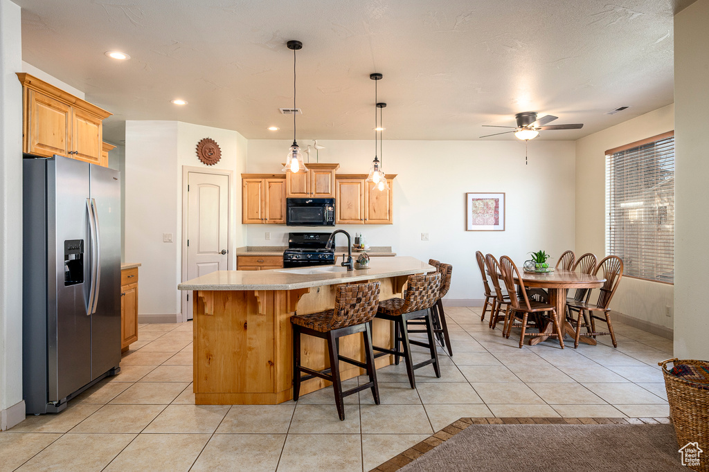 Kitchen featuring light tile patterned flooring, an island with sink, pendant lighting, black appliances, and ceiling fan