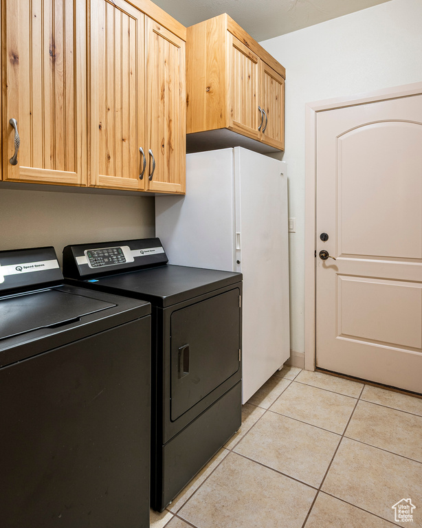 Clothes washing area with cabinets, light tile patterned flooring, and washing machine and clothes dryer