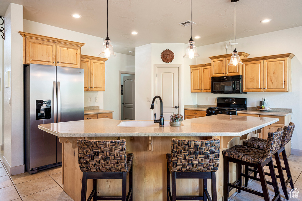 Kitchen featuring pendant lighting, light tile patterned floors, black appliances, a spacious island, and a kitchen bar