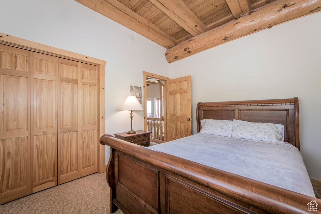 Bedroom with wooden ceiling, beam ceiling, light colored carpet, and a closet