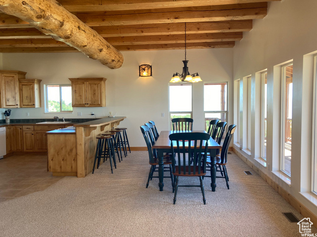 Dining space featuring light tile patterned flooring, a chandelier, beam ceiling, and sink