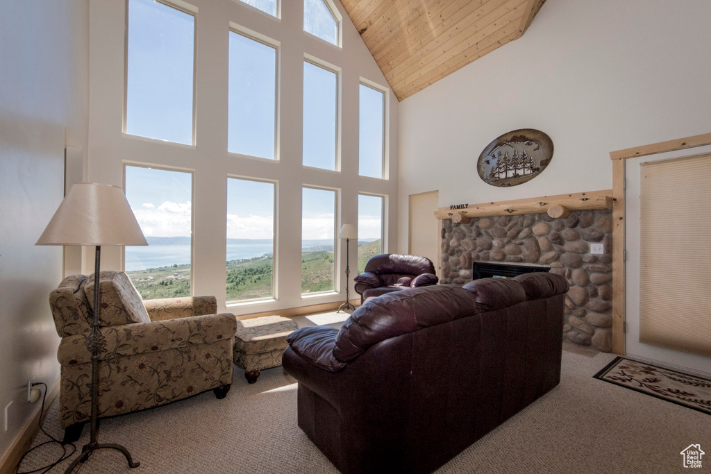 Carpeted living room with wood ceiling, a stone fireplace, a water view, and high vaulted ceiling