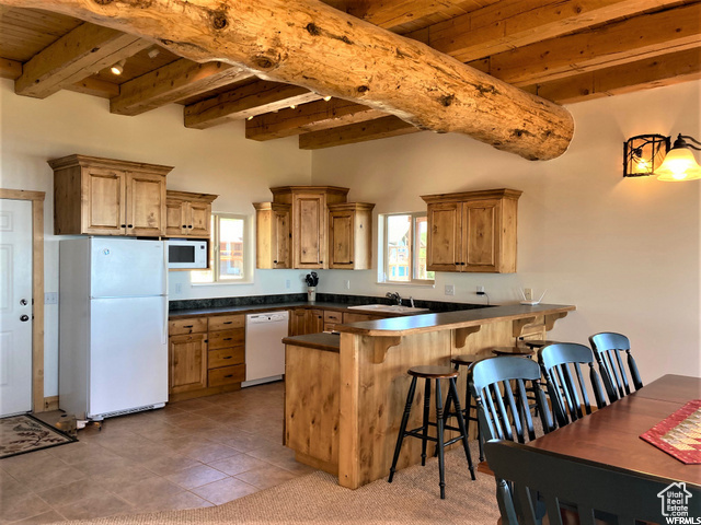 Kitchen with wood ceiling, white appliances, kitchen peninsula, light tile patterned floors, and beamed ceiling