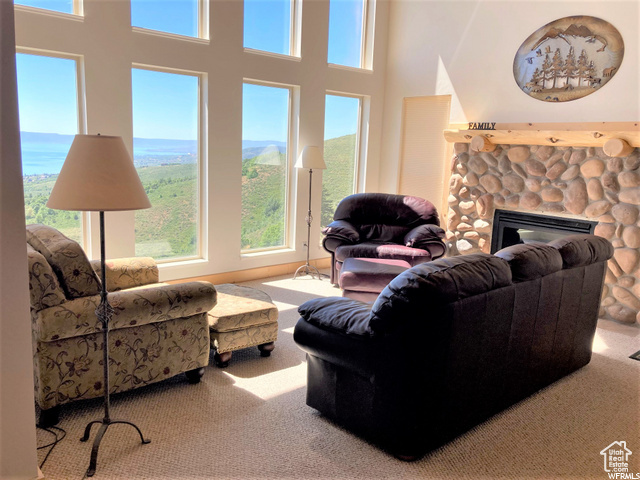 Carpeted living room featuring a stone fireplace, a towering ceiling, and a healthy amount of sunlight